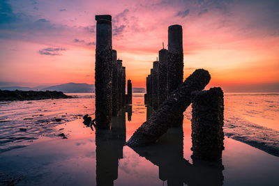 Reflection of wooden post in sea against sky during sunset