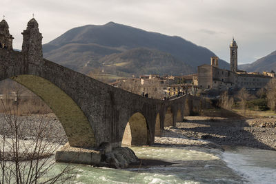 Arch bridge over river amidst buildings against sky