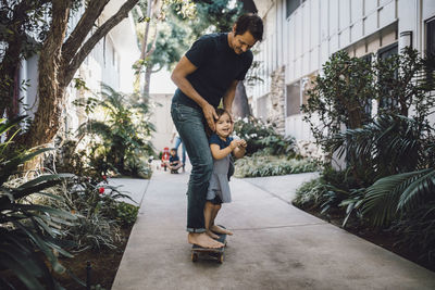 Happy father and daughter skateboarding on footpath