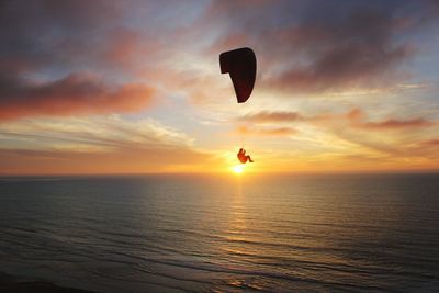 Scenic view of person paragliding during sunset over sea