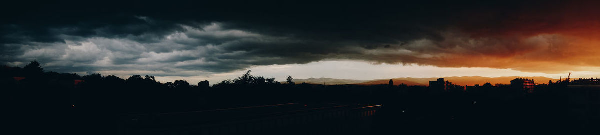 Panoramic view of silhouette trees against dramatic sky during sunset