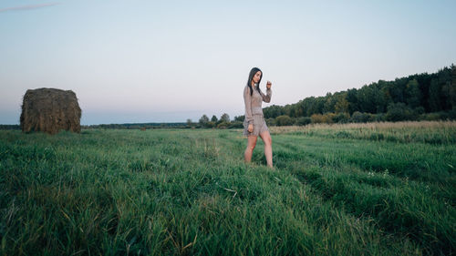 Side view of young woman standing on field against sky