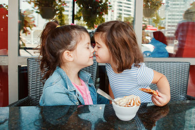 Cute sisters embracing while eating ice cream in cafe