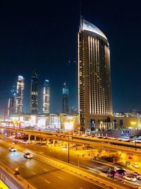 Traffic on road by illuminated buildings against sky at night