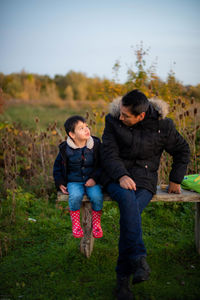 Full length of father and son sitting on a bench in a field