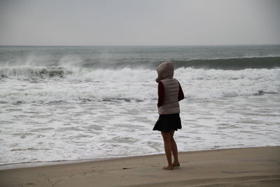 Rear view of woman standing on sea shore against clear sky