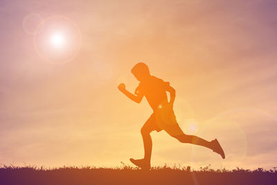 Boy running on field against cloudy sky during sunset