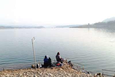 People sitting on lake against sky