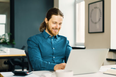 Happy young male office employee working on laptop computer