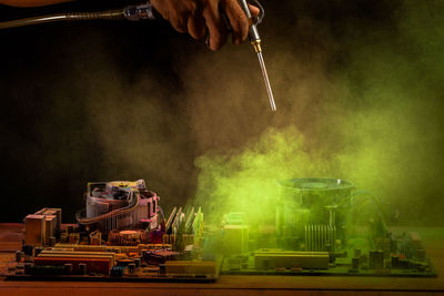 Close-up of man blowing dirt from motherboard on table against black background