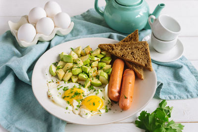 Continental european breakfast of eggs with sausages, toasted rye bread, and cubed zucchini