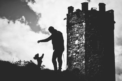 Low angle view of silhouette man feeding dog on field by castle against sky at dusk