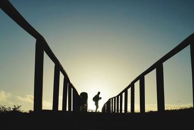 Side view of silhouette man standing on footbridge during sunset