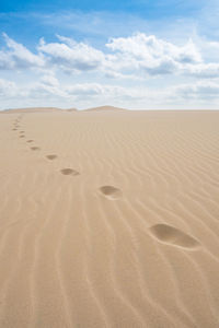 Footprints on sand in desert against sky