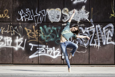 Full length of woman dancing against graffiti on wall