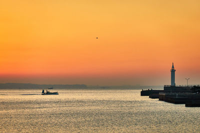 Silhouette ship in sea against orange sky