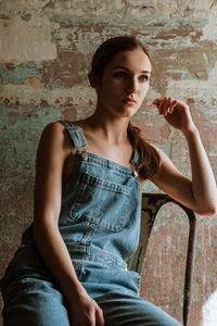 Young woman sitting on chair against wall