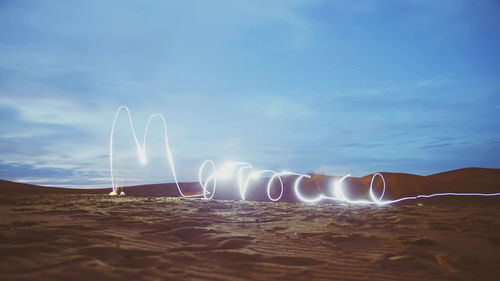 Light trails on beach against sky