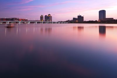 Scenic view of lake by buildings against sky during sunset
