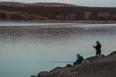 Men fishing on rock by lake