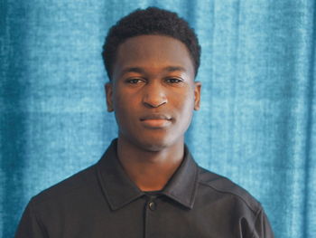 Close-up portrait of young man against blue curtain