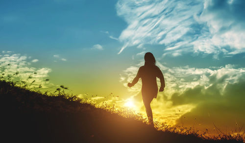 Silhouette woman walking on hill against sky during sunset