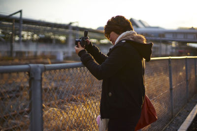 Side view of woman photographing with camera on fence