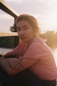 Portrait of woman crouching by railing during sunset