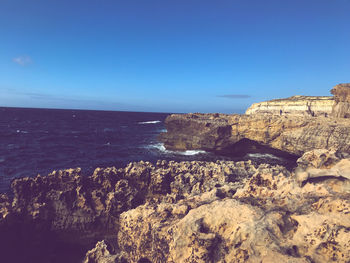 Rock formations by sea against clear blue sky