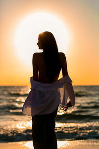 Rear view of man standing at beach against sky during sunset