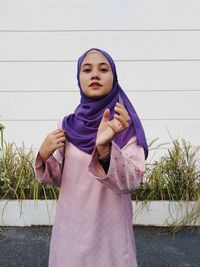 Portrait of young woman standing against wall