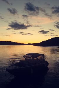 Silhouette boat moored in lake against sky during sunset