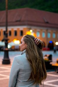 Young woman with long hair standing on walkway in city at dusk