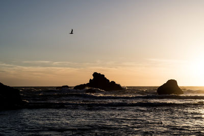 Silhouette rocks on sea against sky during sunset