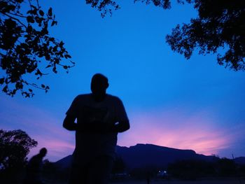 Rear view of silhouette man standing against blue sky