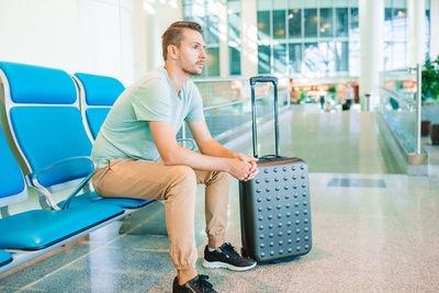 Full length of young man sitting on seat in airport