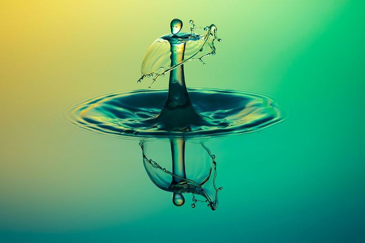 CLOSE-UP OF DROP FALLING ON WATER AGAINST BLUE BACKGROUND