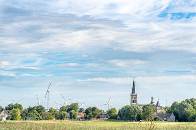 A church in a small town surrounded by wind mills under a blue and cloudy sky