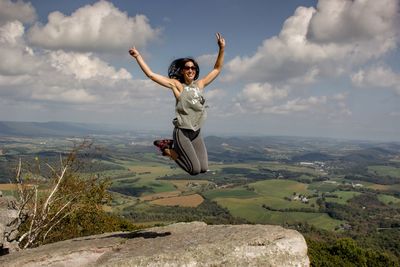 Woman jumping on mountain against sky