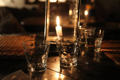 Close-up of empty drinking glass by lit candle on table