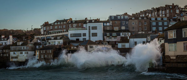 Waves splashing on shore by residential district against sky