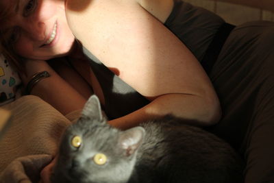 Close-up portrait of cat relaxing on bed with woman at home