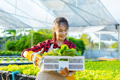 Smiling young woman carrying crate in greenhouse