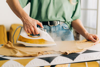 Close-up of an unrecognizable woman ironing clothes with steam on an ironing board.