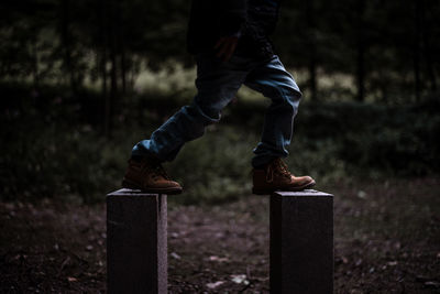 Low section of teenage boy balancing on wooden posts at forest