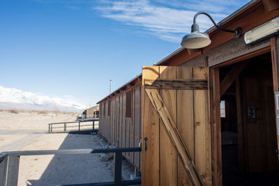 View of wooden open door of barracks amidst buildings against sky