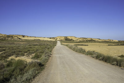 Road amidst land against clear blue sky