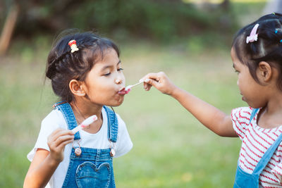 Girl feeding popsicle to sister at park