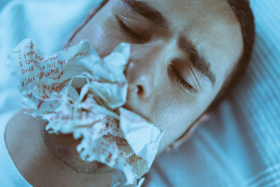 Close-up of young man with eyes closed eating paper while lying on bed at home