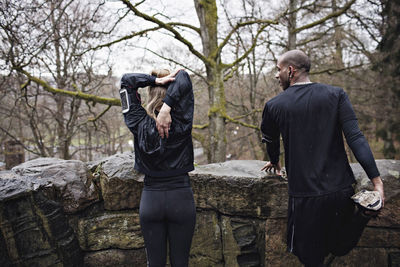 Rear view of male and female athletes doing stretching exercises by surrounding wall